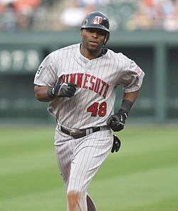 A dark-skinned man running in a grey pinstriped baseball uniform with "MINNESOTA" on the chest in red.