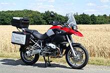 Black, silver and red BMW R1200GS parked on a road by the side of a field of mature wheat