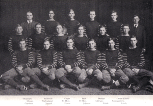Sixteen young men in American football uniform, and two older men in jackets, sitting in three rows.