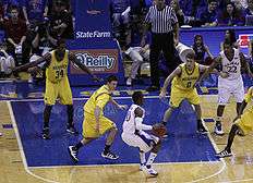 basketball players in maize colored uniforms defend against players in white uniforms