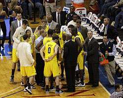 A team of basketball players are standing together in a huddle on a basketball court with their coaches.