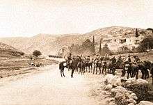 Mounted troopers in the foreground and another group in the middle distance on a road winding between high hills
