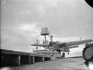 Black and white photograph of a single-engined monoplane running along the deck of an aircraft carrier