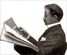A Victorian man of middle age, with a moustache, seated, reading a newspaper, viewed in profile from his left