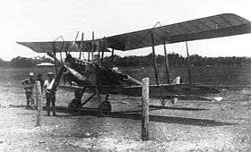Biplane on landing ground with two men beside it