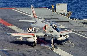 A small, single-seat jet fighter has just touched down on the flight deck of an aircraft carrier