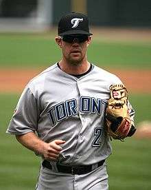 A man in grey a baseball uniform with "Toronto" and "2" on the jersey and a black cap with the Toronto Blue Jays logo on it.