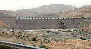 A gently curving concrete dam in an arid, mountainous area.