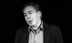 Black-and-white portrait of a man in his fifties in a dark suit jacket and light shirt, mid-speech with his head tilted slightly to the left, looking to the left of the camera.