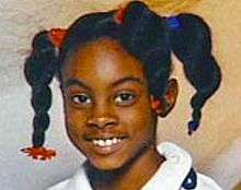A young girl with dark brown skin and braided black hair, smiling