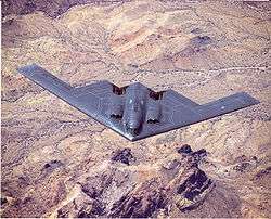 Top view of triangular aircraft, with sawtooth trailing edge, in flight over desert