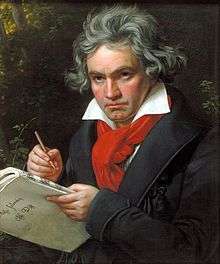 A man with long grey hair holding a pen and music paper