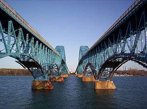 Twin spans of the South Grand Island Bridge, which cross the Niagara River in five sky-blue steel arches. The central arch is above the roadway permitting passage of large freight ships.