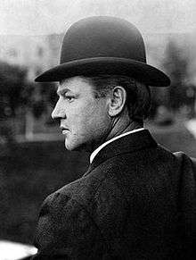 A man wearing a bowler cap, in profile.