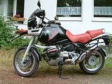 Black BMW R1100GS with red seat parked on dirt in front of a house
