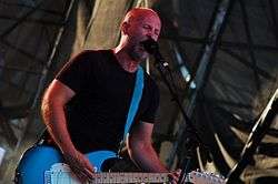 A bald man sings and plays a guitar on stage.