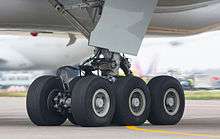Aircraft landing gear. Six wheel gear on the ground, with attachment assembly and gear door leading up to the aircraft belly.