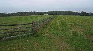 Photo of a gently sloping cleared field along a fence line with trees in the distance