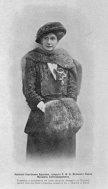 Three-quarter length portrait photograph of a lady wearing an Edwardian-style dress and hat with furs