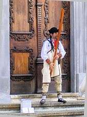 A man playing the fujara instrument in front of a large wooden door