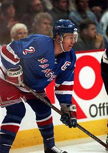 An ice hockey player on the ice, bent over. He is in a blue jersey with the word "Rangers" across the front of his jersey.