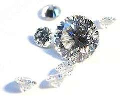 Several white diamonds with brilliant cuts lie scattered across a white background.