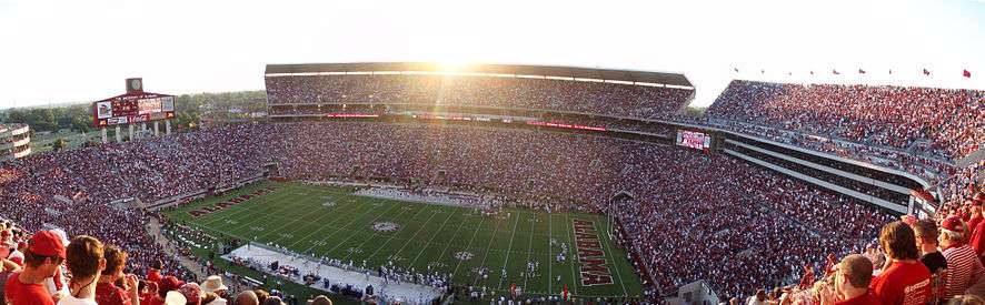 A setting sun with the interior of Bryant-Denny Stadium full of fans and players on the field.