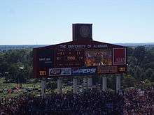 Large scoreboard in an American football stadium surrounded by crowded stands.