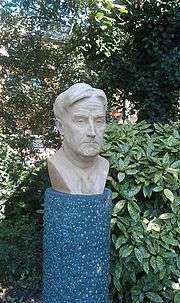 Outdoor bust of middle aged man with good head of hair, against a garden background