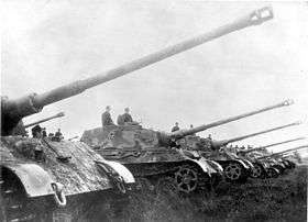 A row of seven large tanks lined up with their long guns pointing up at an angle, as if saluting.
