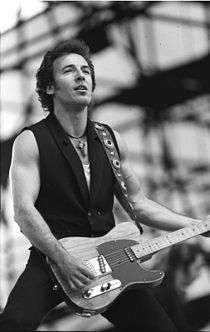 A black and white photograph of Bruce Springsteen on stage with a guitar