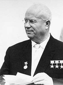 An elderly bald man in a suit, with several medals pinned on it