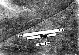 Overhead view of single-engined military biplane with twin-tail boom in flight