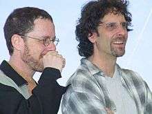 Two men in button-up shirts smiling.