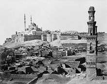A multi-domed mosque dominates the walled Citadel, with ruined tombs and a lone minaret in front.