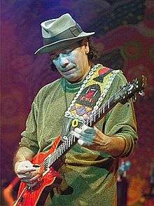 A man wearing a grey hat and a green sweater playing the electric guitar.