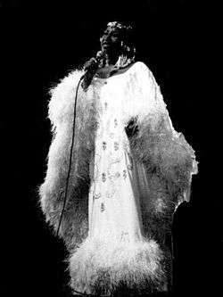 A woman in a white feathers' dress holding a microphone up her neck.