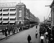 Masses of men throng the streets outside a building.