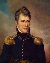 A man with graying, wavy hair wearing a high-collared black military jacket with gold epaulets and buttons