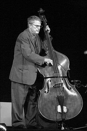 Black and white image of a man in a suit playing on a bass (a large string instrument).