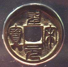 A circular golden coin with a square hole in the center and four Chinese characters, one to each side of the hole, embossed into the body of the coin.