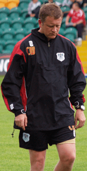 A man is looking down at the ground while walking, wearing a tracksuit top and shorts
