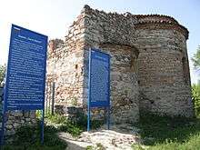 Southeast view of a church. Two of the three apses are visible, the middle one larger than the side ones. Blue signs with information in Bulgarian and English next to the building.