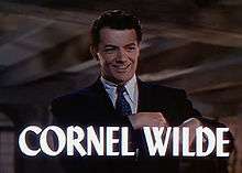 Frame of a film. A man wearing a suit and tie is smiling towards the camera. The words "CORNEL WILDE" are superposed on the image across the bottom of the frame.