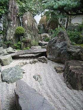 Rock garden with raked gravel and large stones including one placed like a bridge.