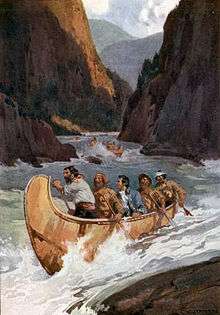 Men in canoes descend wild rapids in a river canyon.