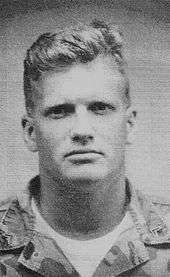 Head shot of a young, blond Carey dressed in military fatigues.