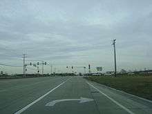 Approaching intersection with IL 60. Road is 2 lanes in each direction, concrete lanes. Traffic signal lies ahead from viewpoint of right turn lane.