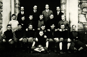 A black and white photograph of eighteen male student members dressed in football gear