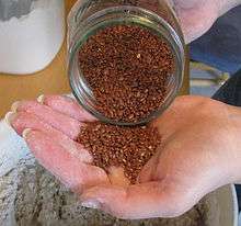 Flaxseed is poured from a jar into the hand.